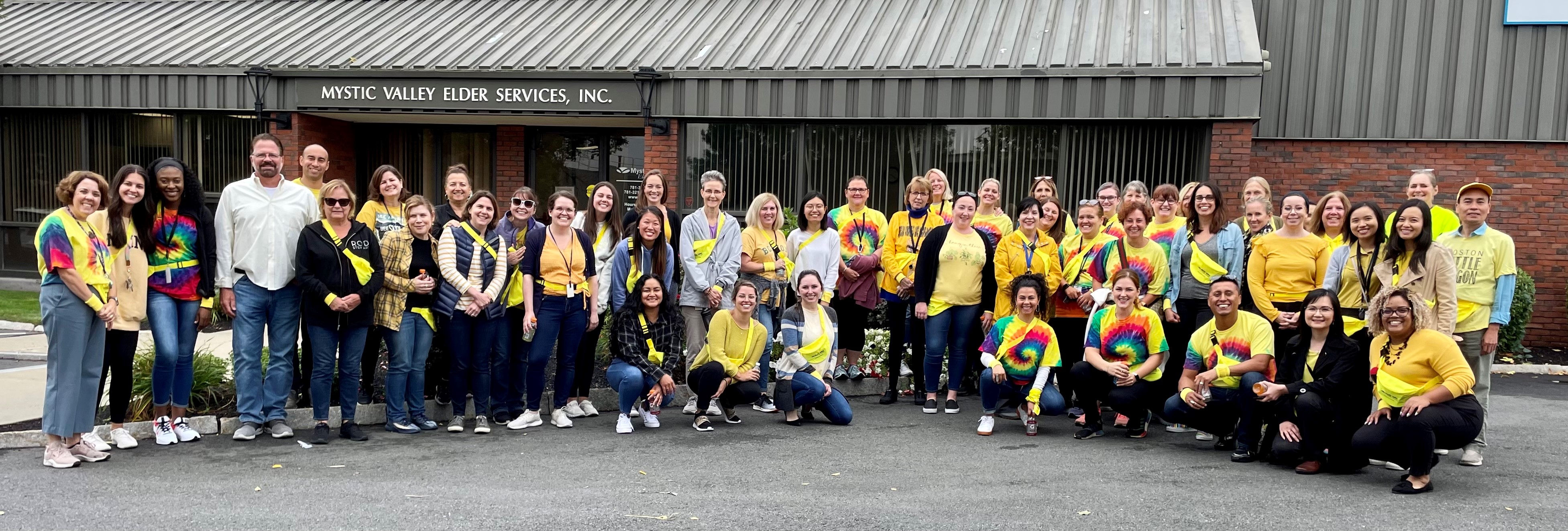 large group of coworkers posed in front of the workplace, wearing yellow for an event