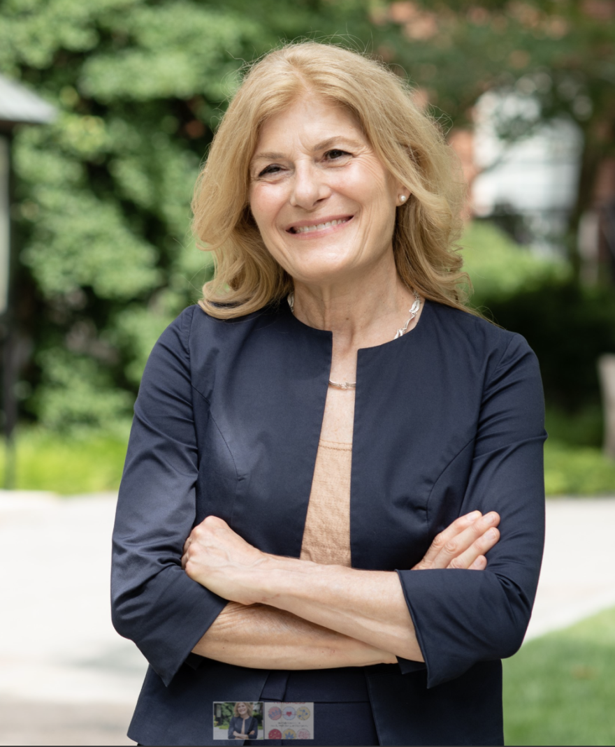 Author Dr. Immaculata De Vivo, photographed in a park, wearing a black and tan business-type outfit.