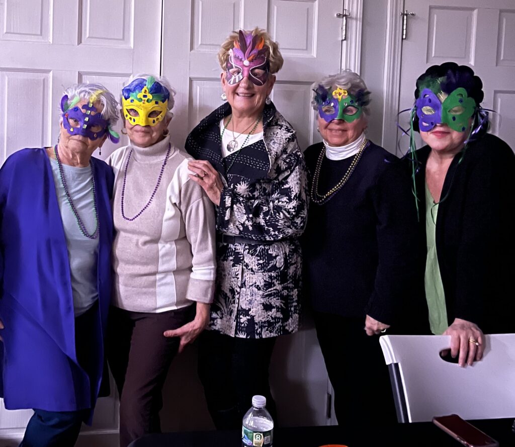 5 older adults in Melrose, all women, pose in a row. They are wearing colorful Mardi Gras style masks that cover the tops of their faces.