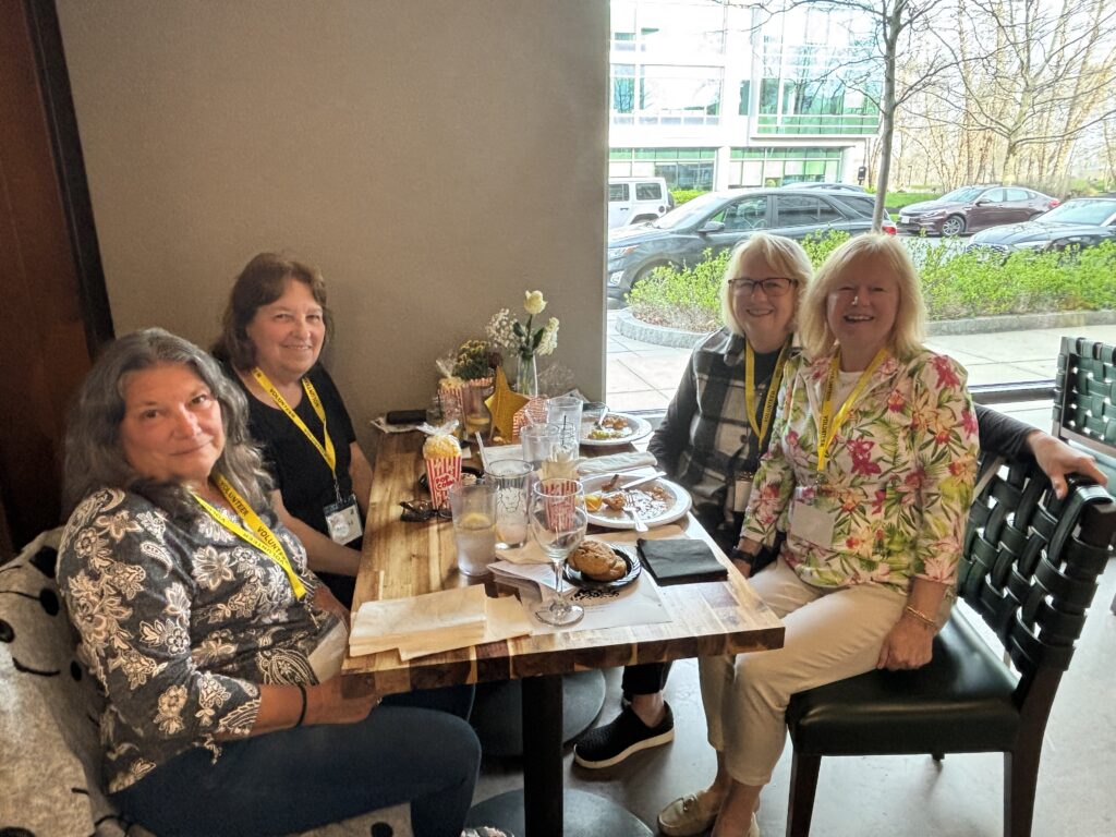 Four women wearing yellow volunteer lanyards smile while seated at a table with decorations and dinner.