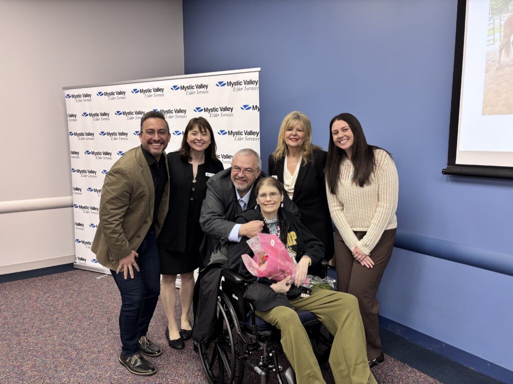 Several MVES Board and staff surround Frank and Colleen, who the agency is assisting. Colleen is in her wheelchair holding a bouquet of flowers.